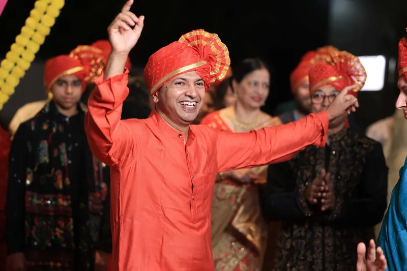 Man in an orange kurta and pheta dancing with arms raised
