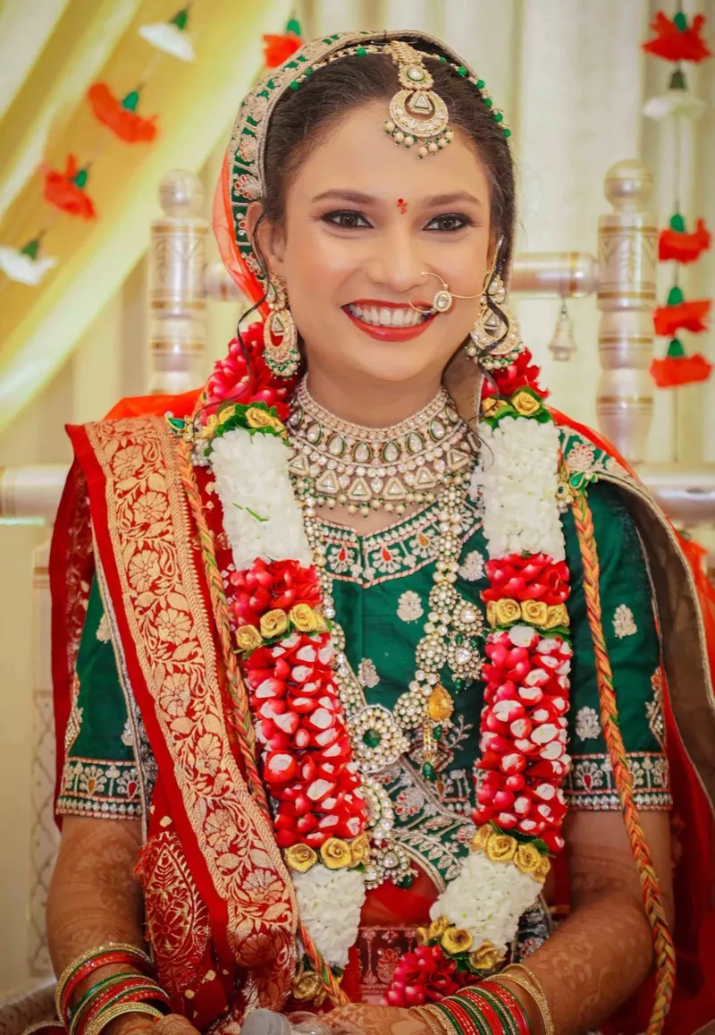 Bride in a green and red saree smiling, wearing a rose and tuberose varmala