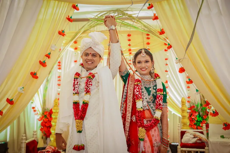 Couple laughing with joined hands raised under a floral mandap