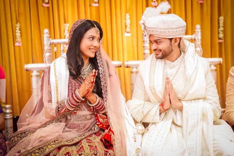 Bride and groom seated side by side on the mandap, groom folding his hands in greeting