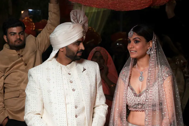 Groom in ivory sherwani and safa beside the bride at an evening reception