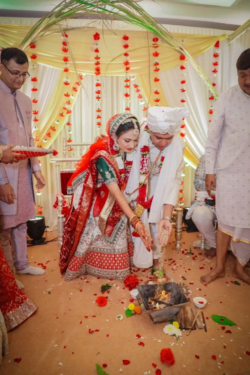 Bride and groom offering rice to the sacred fire during the pheras, family watching