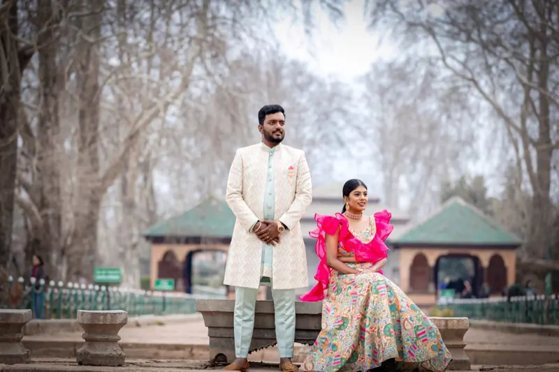 Couple in festive outfits posing among bare chinar trees on a misty morning